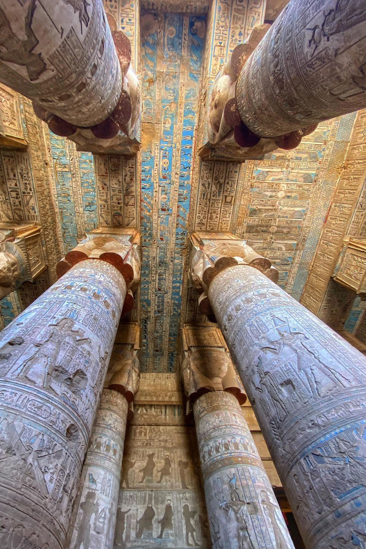 A view of the ceiling of the Dendera Temple in Egypt filled with blue hieroglyphs and supported by enormous columns. 