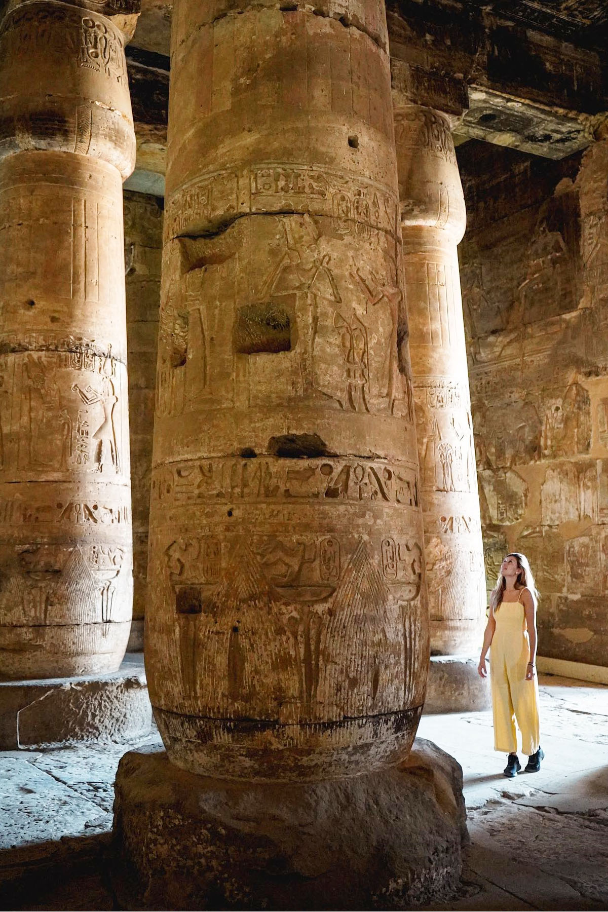 Enormous columns at the Abydos temple in Egypt with a woman walking through looking up.