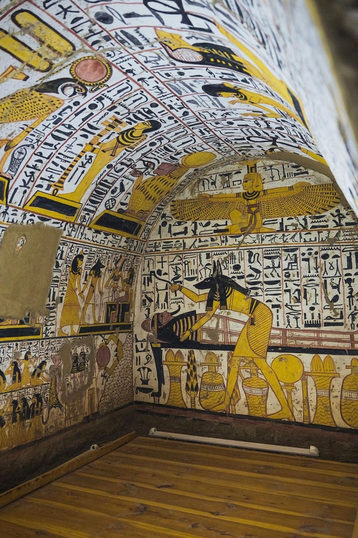 A colorful tomb inside Deir el Medina in Luxor is colored in hieroglyphs and yellows that depict Egyptian gods and a funerary scene of mummification.