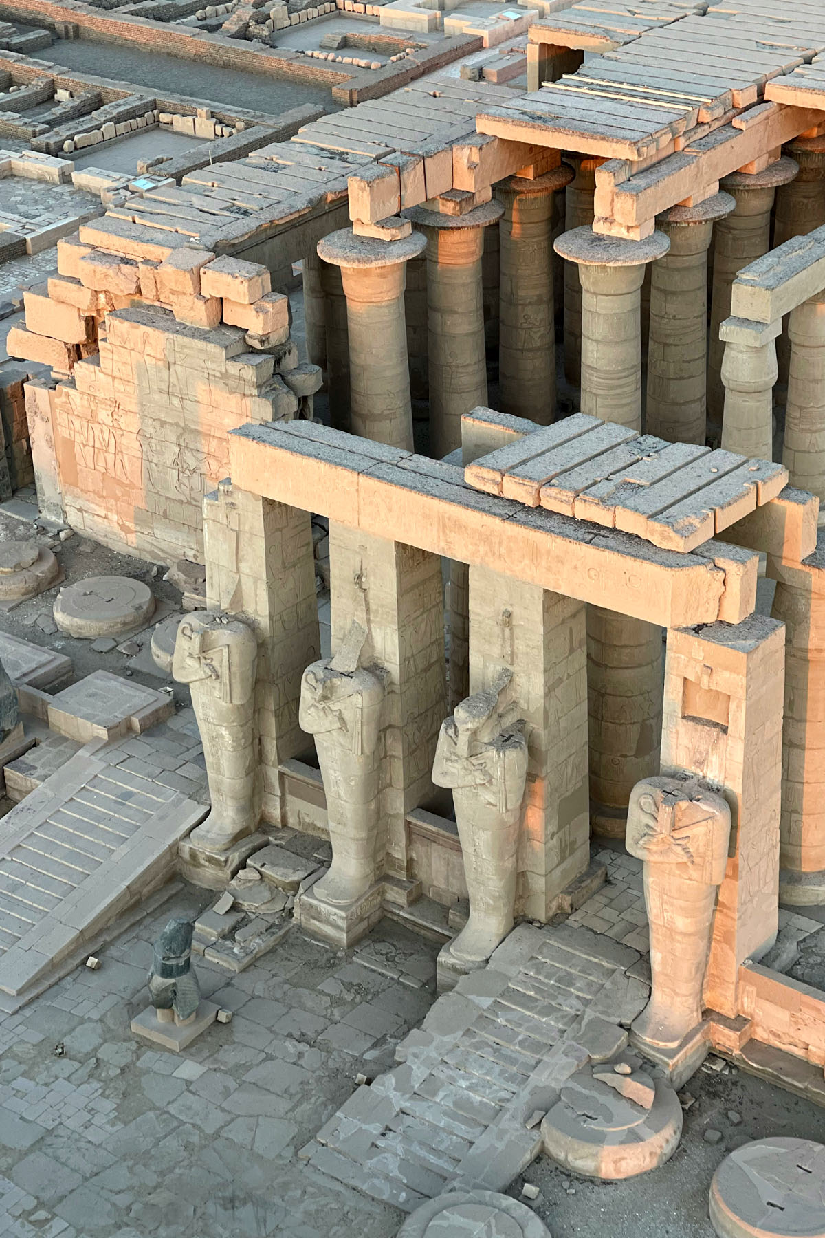 A bird's eye view of the Ramesseum in Luxor shows enormous statues with missing heads in the front of rows of tall columns. 