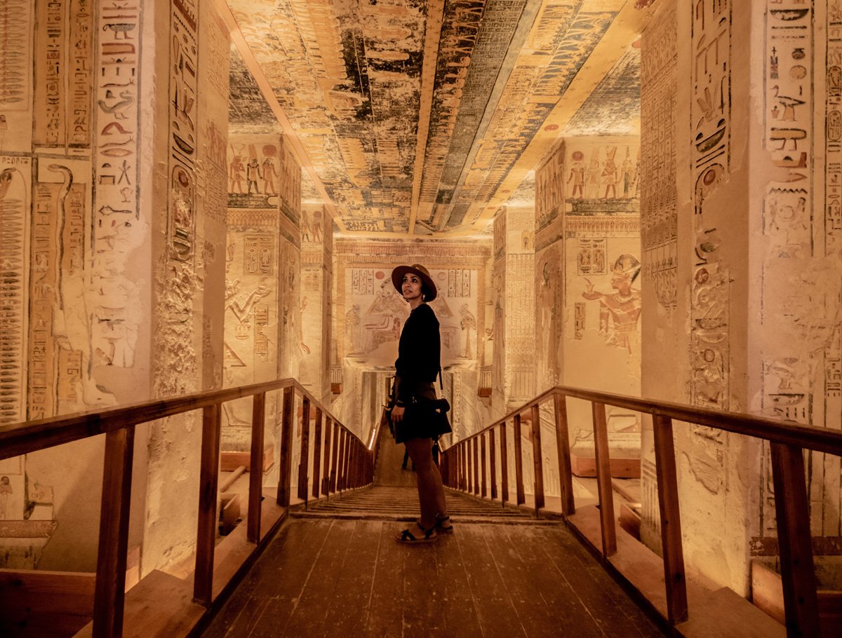 A woman stands in the passageway inside a tomb inside the Valley of the Kings in Luxor. The passage is narrow and the walls are decorated entirely with hieroglyphs. 