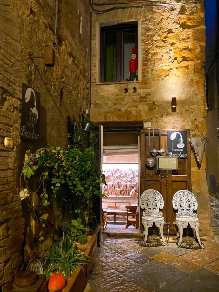 Charming entrance to Ristorante Beccofino in Pienza, Tuscany at night with vintage white chairs and rustic decor