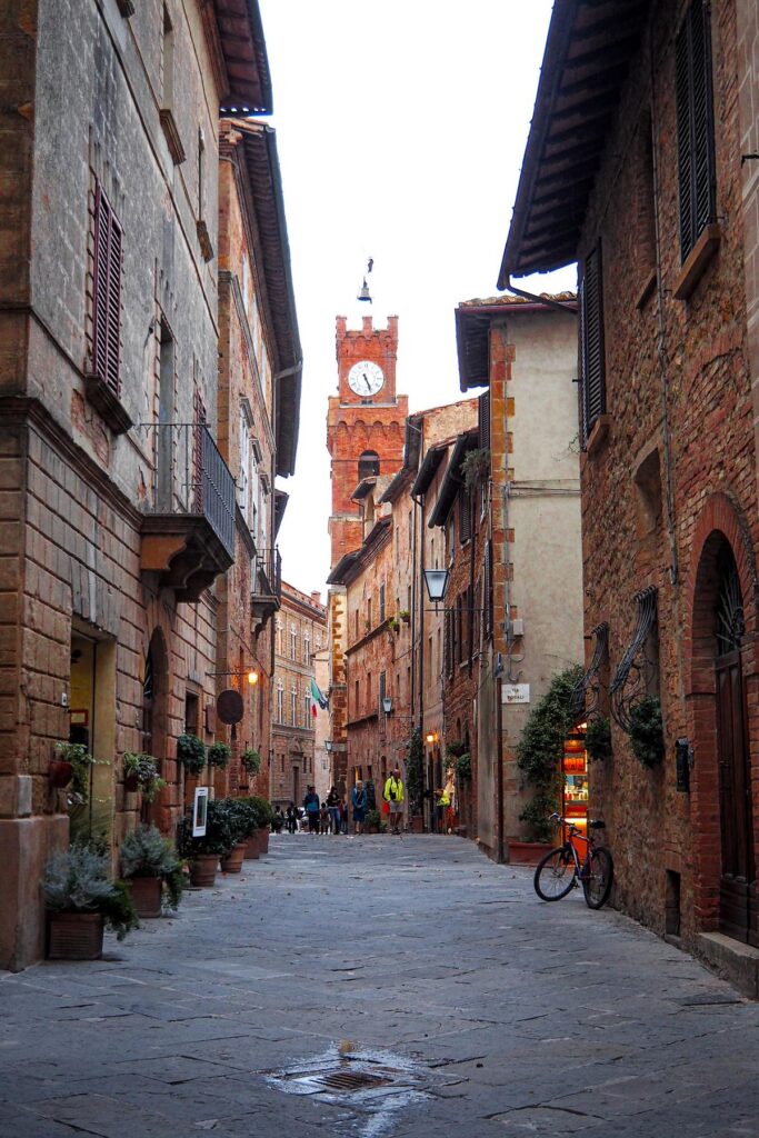 Cobblestone street with historic buildings in Pienza, Italy, featuring traditional architecture and warm ambient lighting.