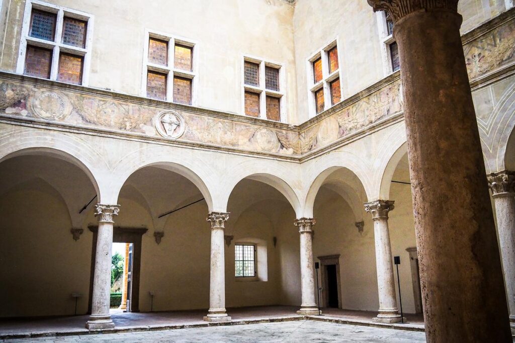 Architectural splendor of Palazzo Piccolomini, Pienza: elegant porticos, frescoes, classical columns, stained glass windows in vivid color space.