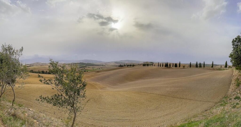 Tuscan countryside of Val d'Orcia panorama with rolling hills, cypress trees, and dramatic clouds