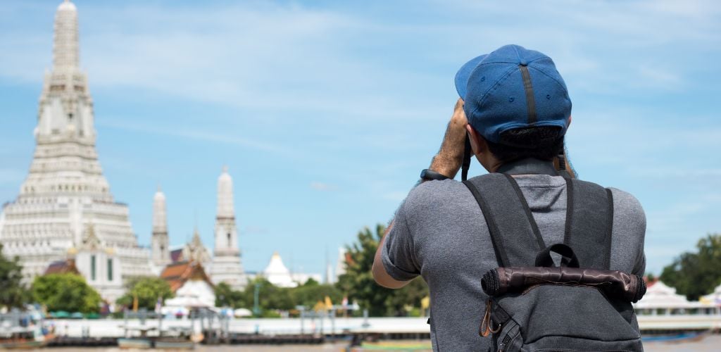 Traveling tourist/digital nomad taking a photo at Wat Arun Temple in Bangkok Thailand.