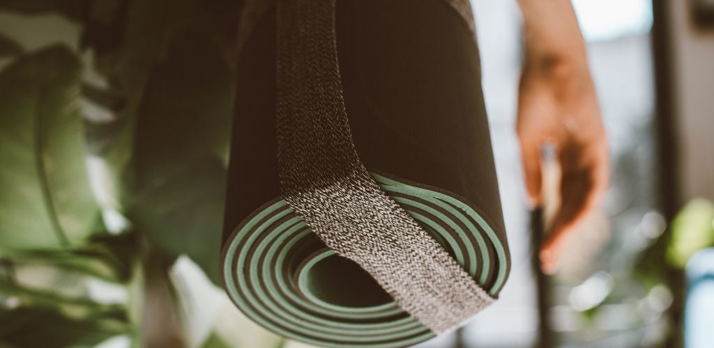 rolled yoga mat over shoulder, walking through jungle 