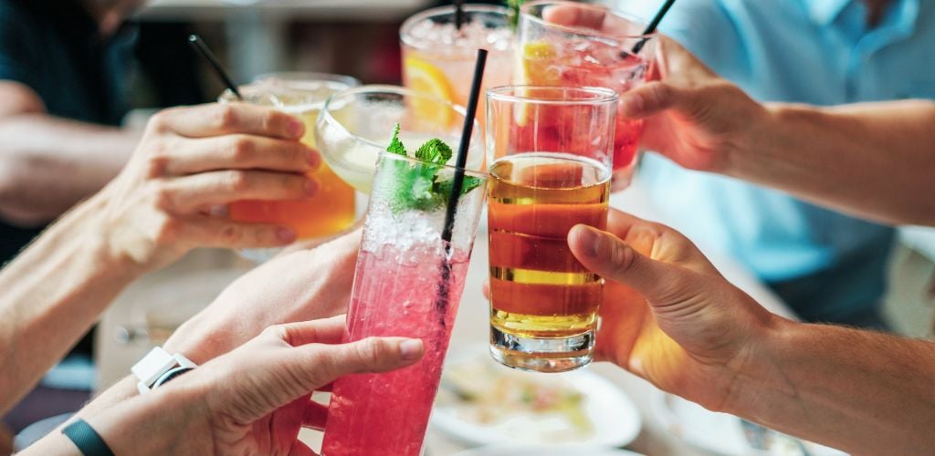 group of friends cheers with drinks, mix of cocktails and and beers in outdoors space 