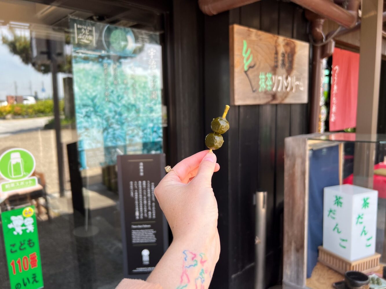 Female traveler holding miniature matcha dango rice cakes on a skewer in Uji, Japan.