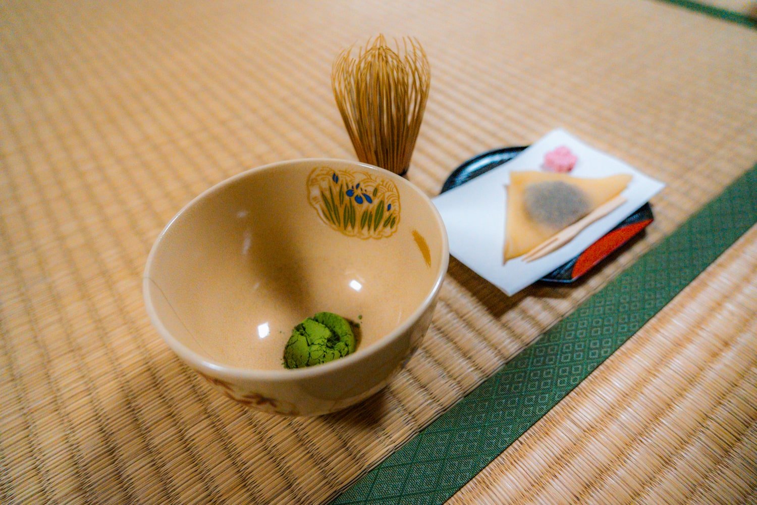 Japanese tea ceremony with bowl of matcha powder and plate of higashi and omogashi.