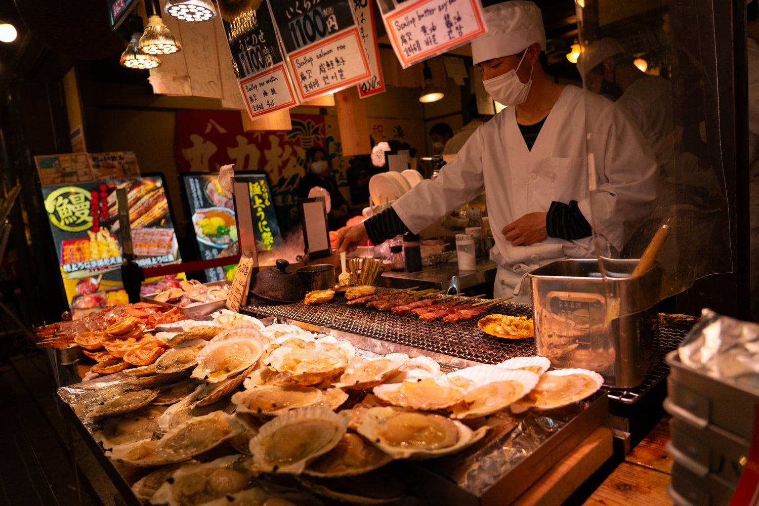A chef prepares Japanese food such as oysters and yakitori on an outdoor grill at the Nishiki Market in Kyoto.
