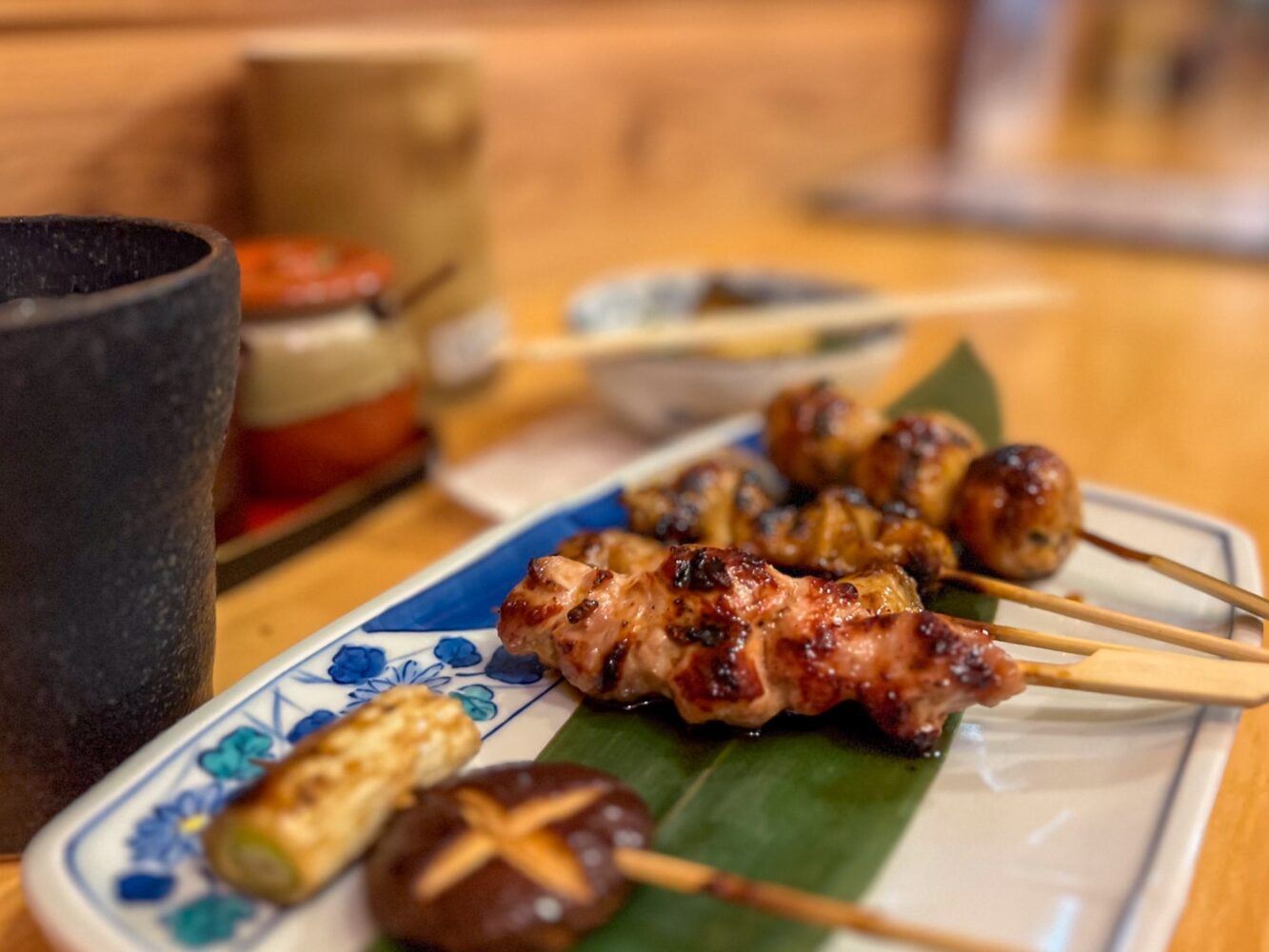 Japanese yakitori on a plate inside a traditional izakaya pub, featuring different types of chicken meat on bamboo skewers.