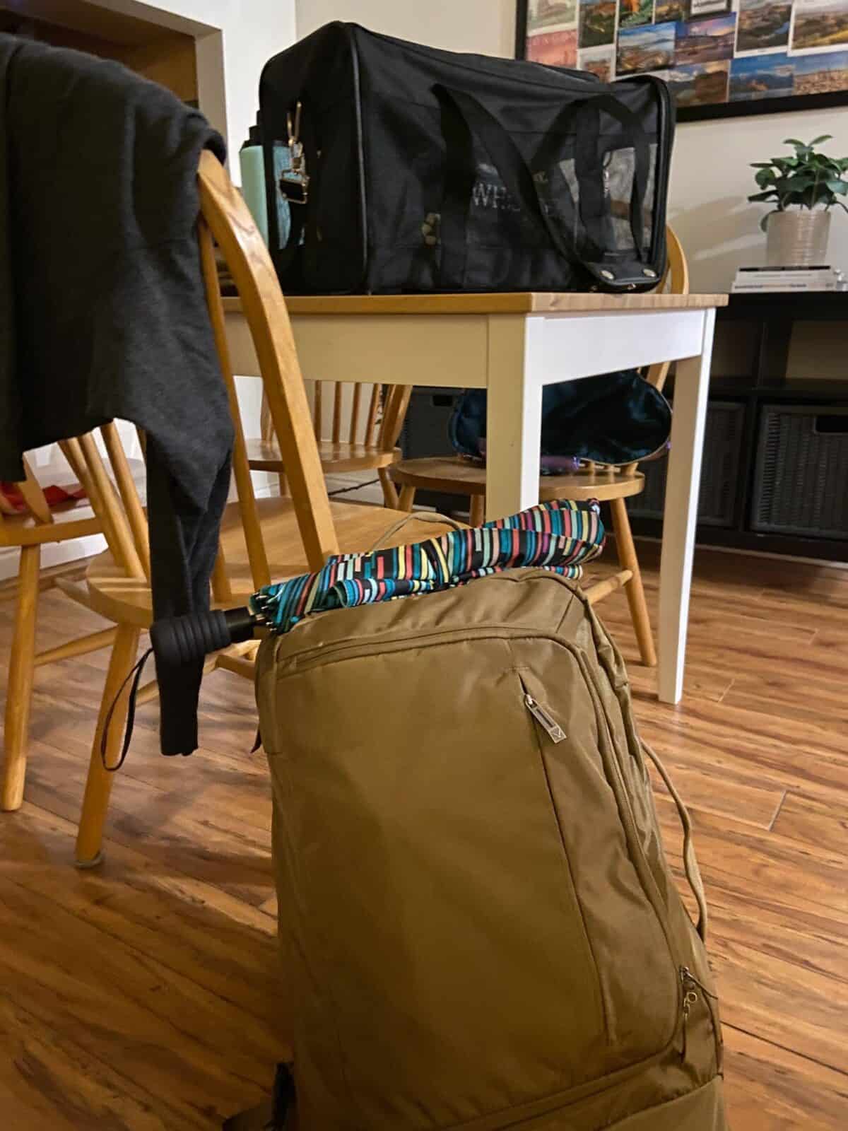My carry-on backpack sitting on the floor with an umbrella perched on top, packing hacks and mistakes