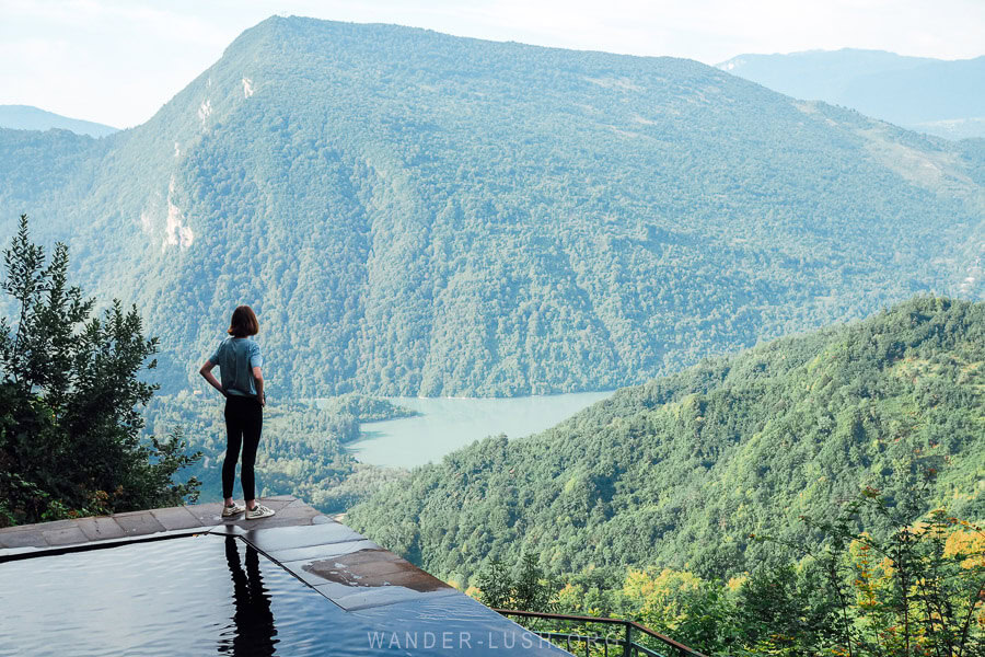 A person stands beside a mountain pool surrounded by green hills. Lailashi Secret Pool in Georgia.