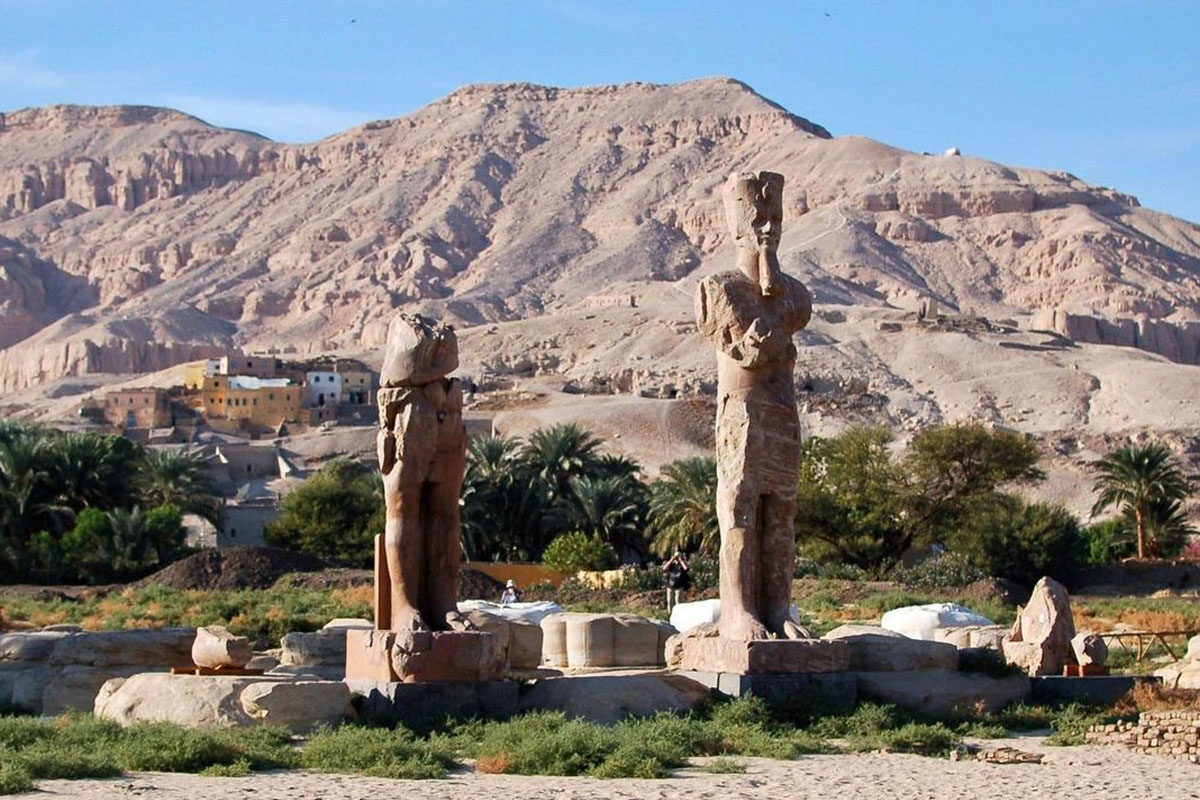 Statues stand in the grass with hills behind them at the temple of amenhotep III in luxor, just beyond the Colossi of Memnon.