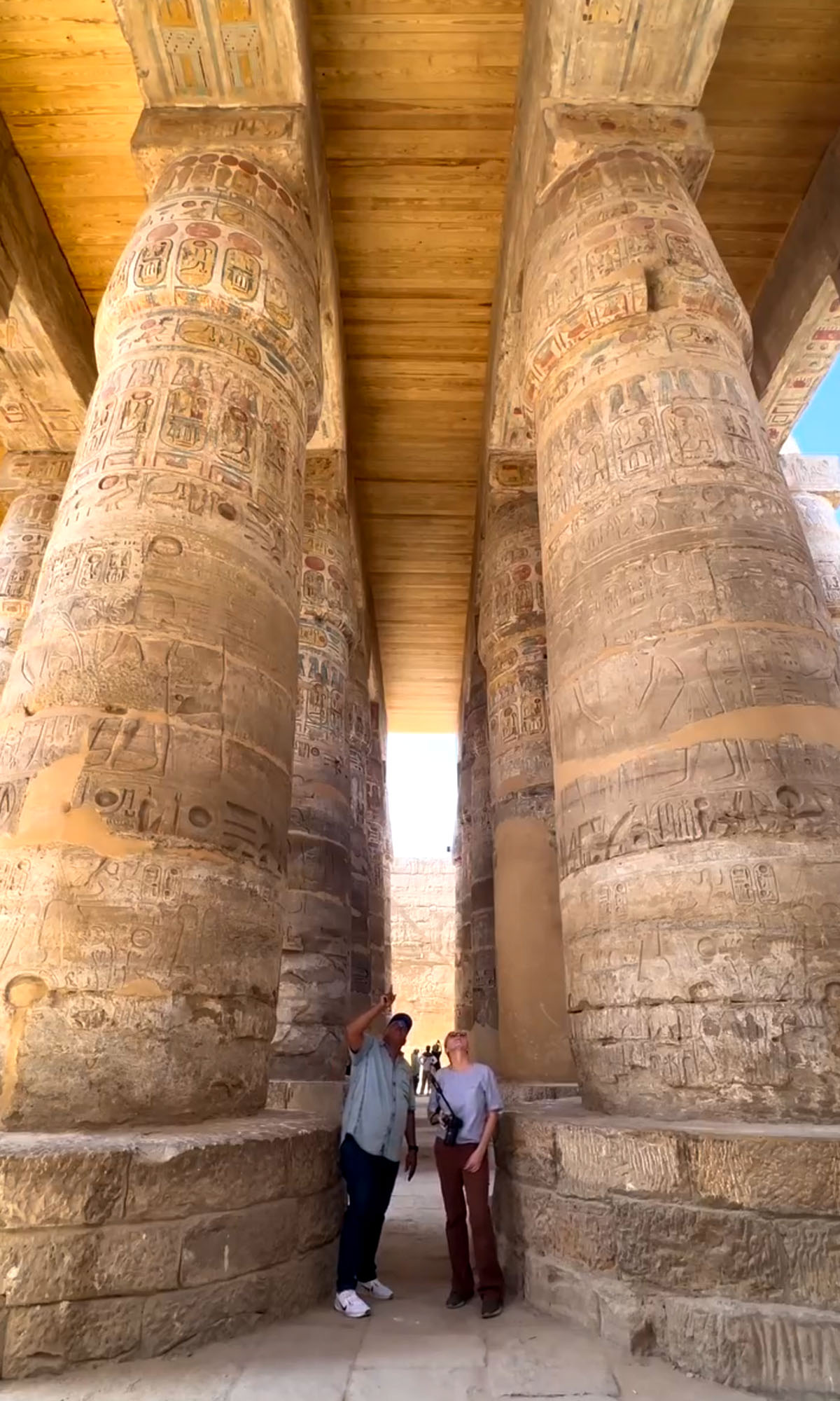 The enormous tall columns line the hypostyle hall inside Karnak Temple in Luxor. Dee stands at the base of the columns with her tour guide holding a camera. 