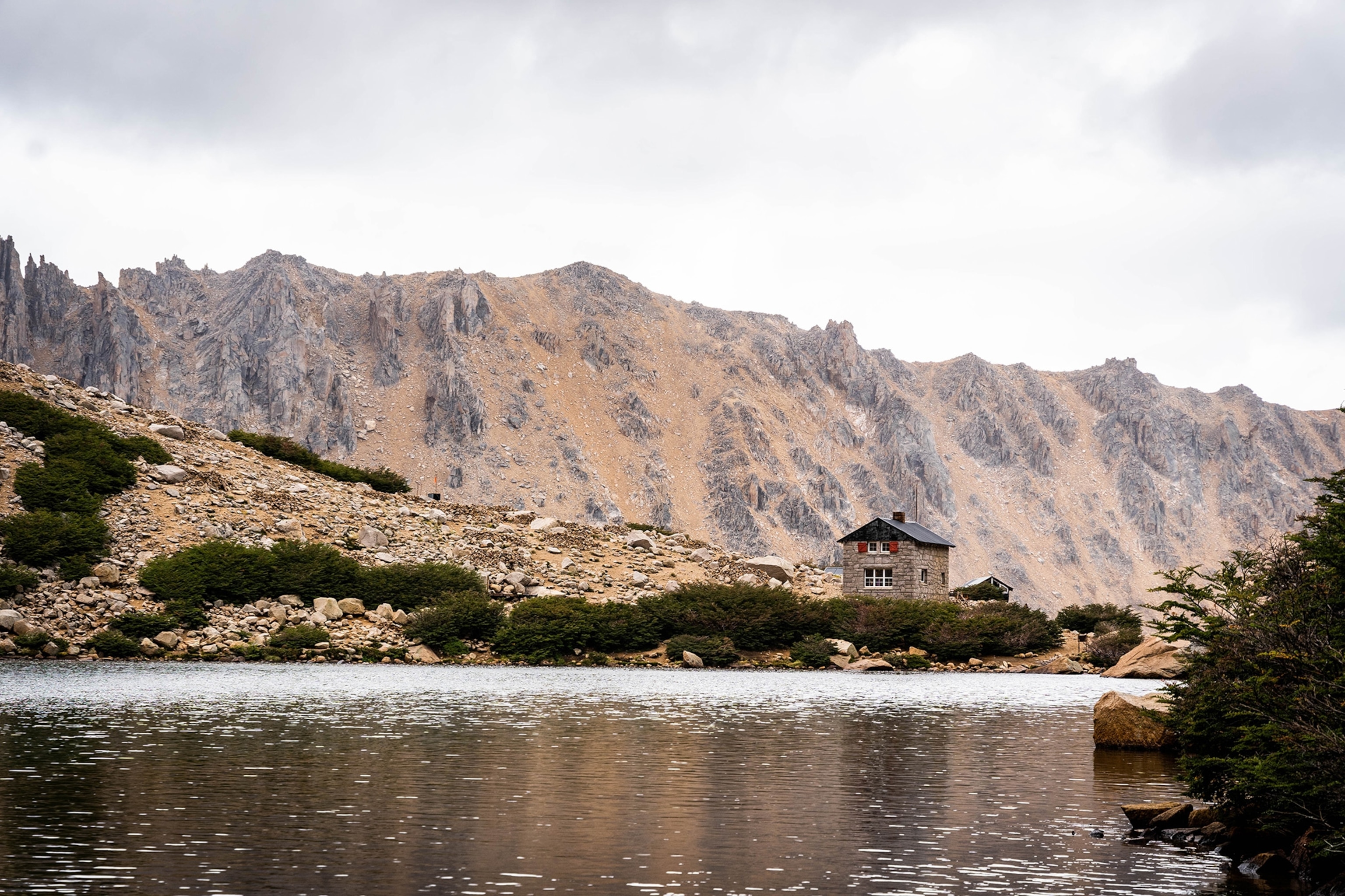 A small house overlooks a lake surrounded by a mountain.