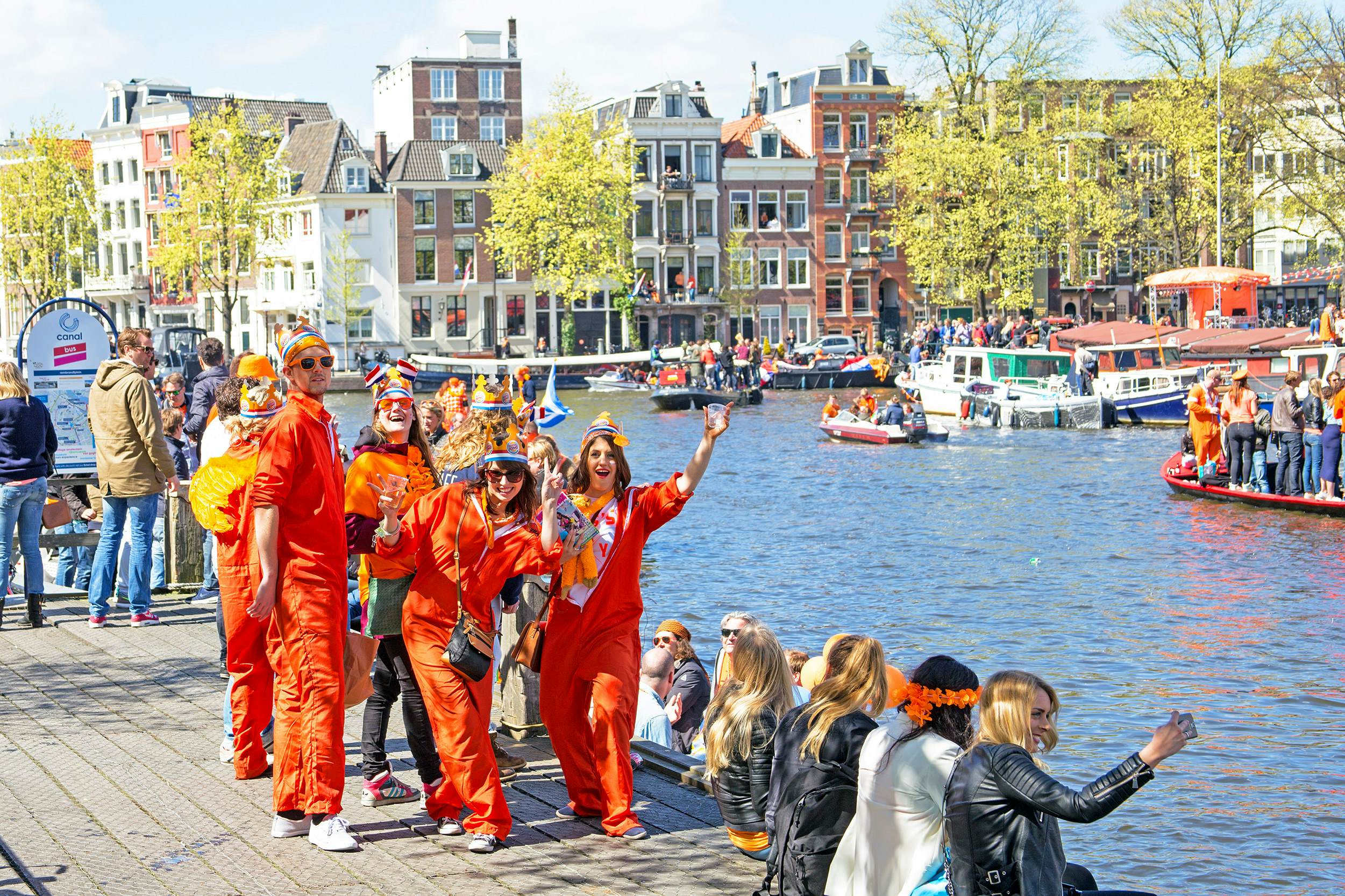 People dressed in orange celebrate near a canal in a city