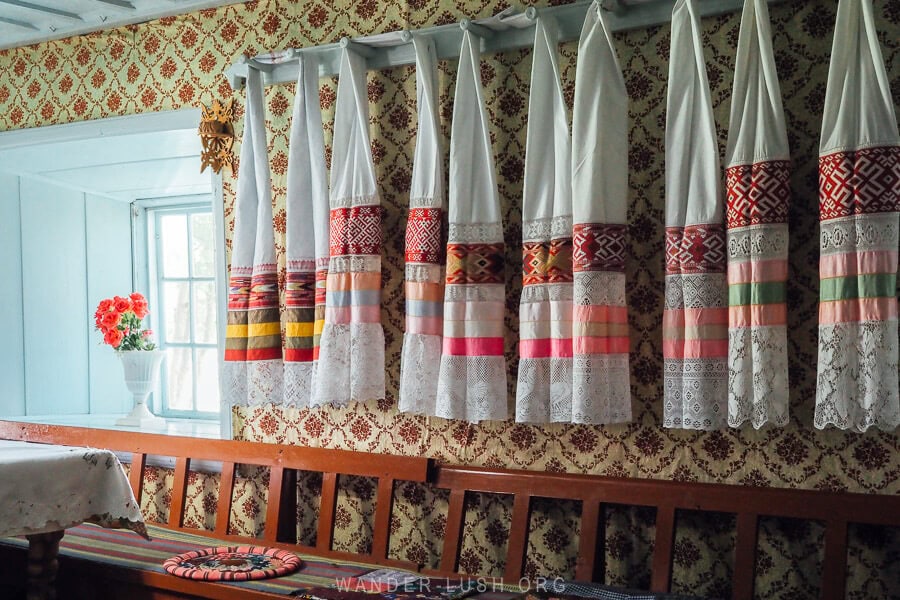 Traditional scarves with embroidery and lace hanging above a long wooden bench inside the Prayer House in Gorelovka, Georgia.