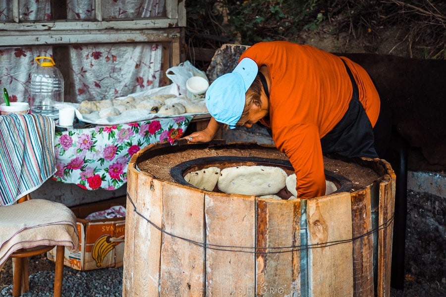 A woman reaches into a clay oven whilst baking nazuki, a sweet bread in Surami, Georgia.