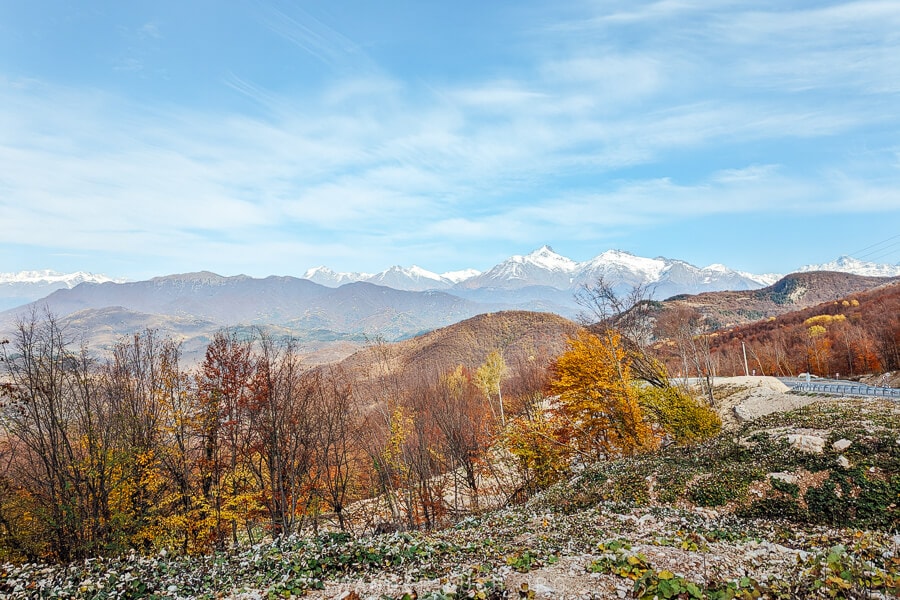 A scenic mountain road in Racha, with snow-capped peaks and fall colours.