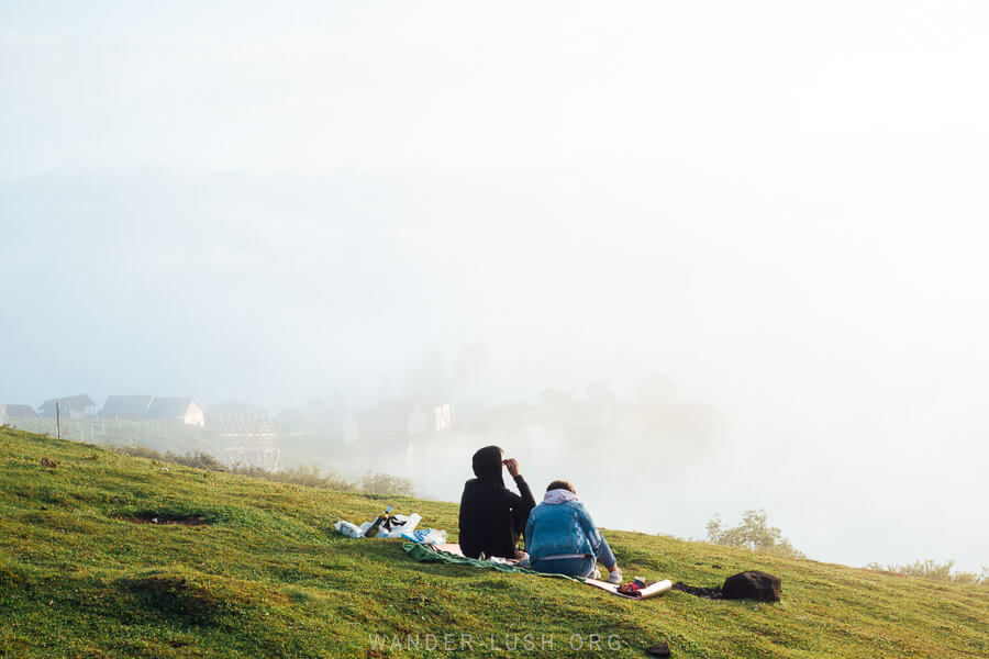 Two people sit on a rug and look out into the foggy distance atop Gomismta mountain in Guria.