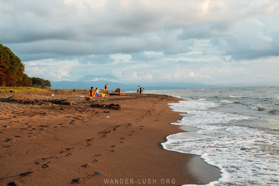 People sit on the shore of a black-sand beach in Georgia.