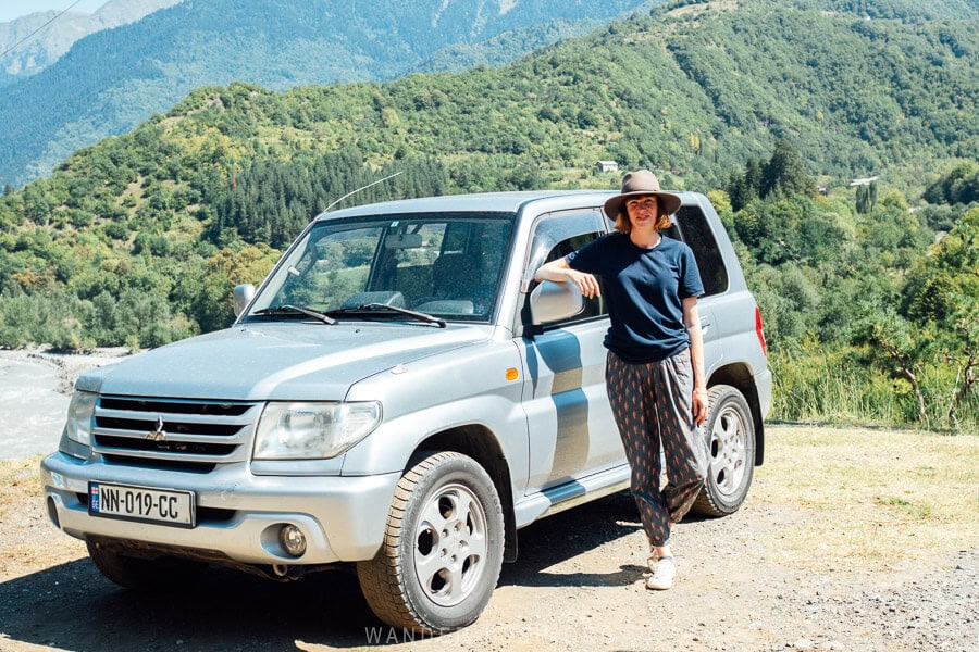 A woman stands with a 4WD on a mountain road in Racha, Georgia.