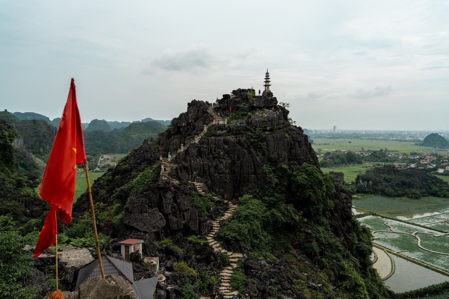 Hang Mua Cave Pagoda viewpoint with Vietnamese flags and staircase leading up to Ngao Long Mountain.