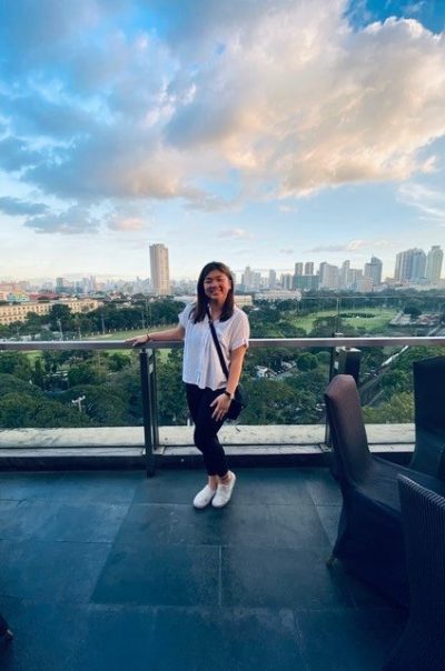 Sarah standing on a balcony with a skyline behind her.