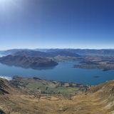 Panoramic photo of New Zealand including a lake with dark blue water and several small islands throughout.