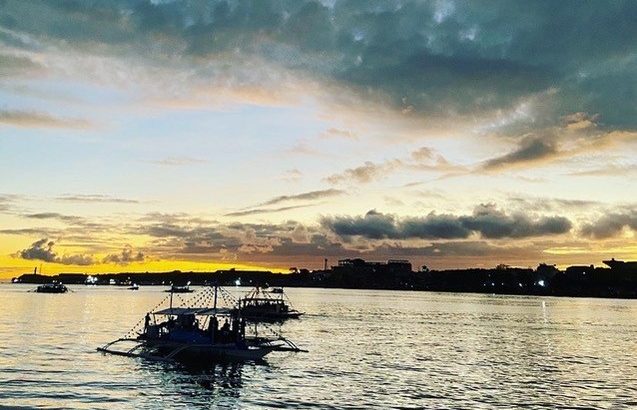 The ocean while the sun is setting. Some boats are spread out across the water and the water looks dark.