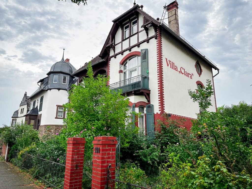 Villa Clara, Weingut George vineyards, Germany - traditional estate with lush greenery, ivory facade, Villa Clara script, and unique turret, surrounded by garden.