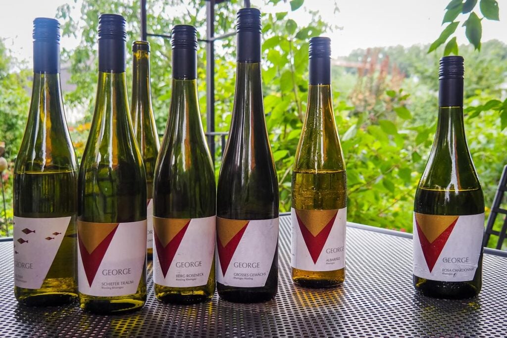 Vibrant collection of white wine bottles from Weingut George displayed on an outdoor tasting table with lush greenery in the background.