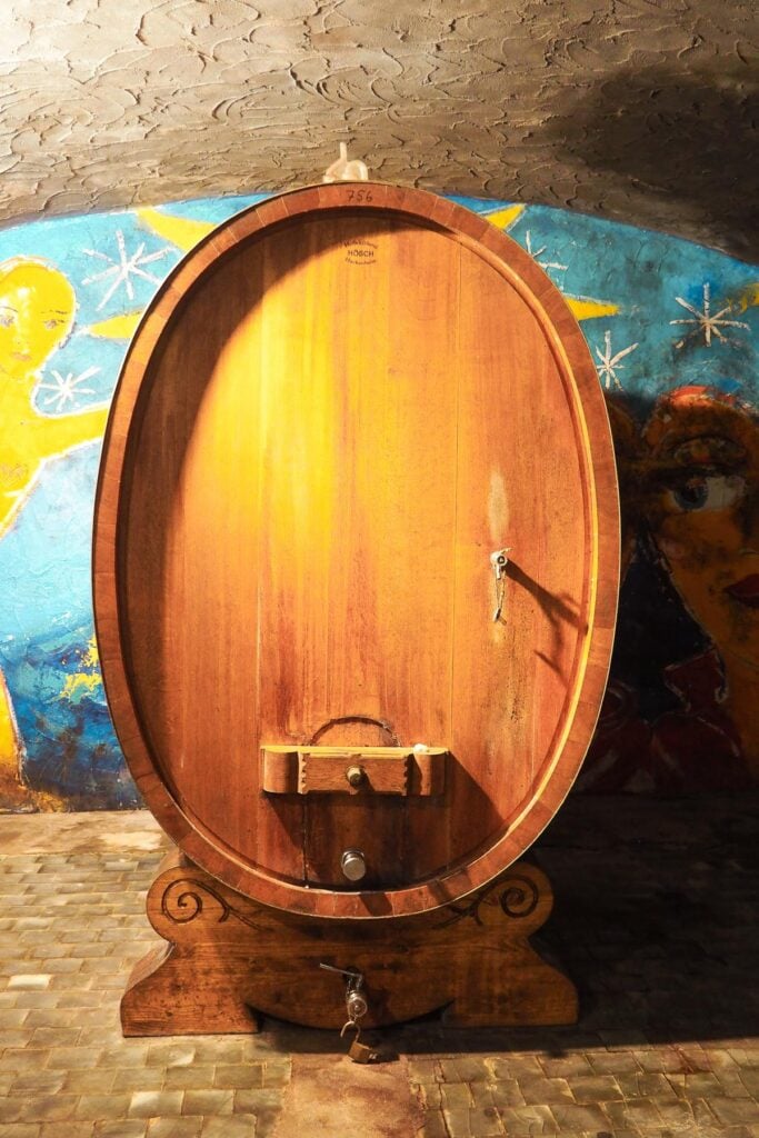 Historic oak wine barrel at Weingut Georg Breuer, Germany, with ambient lighting, whimsical wall murals, and intricate '756' and 'HOSCH' markings, showcasing tradition and craftsmanship.