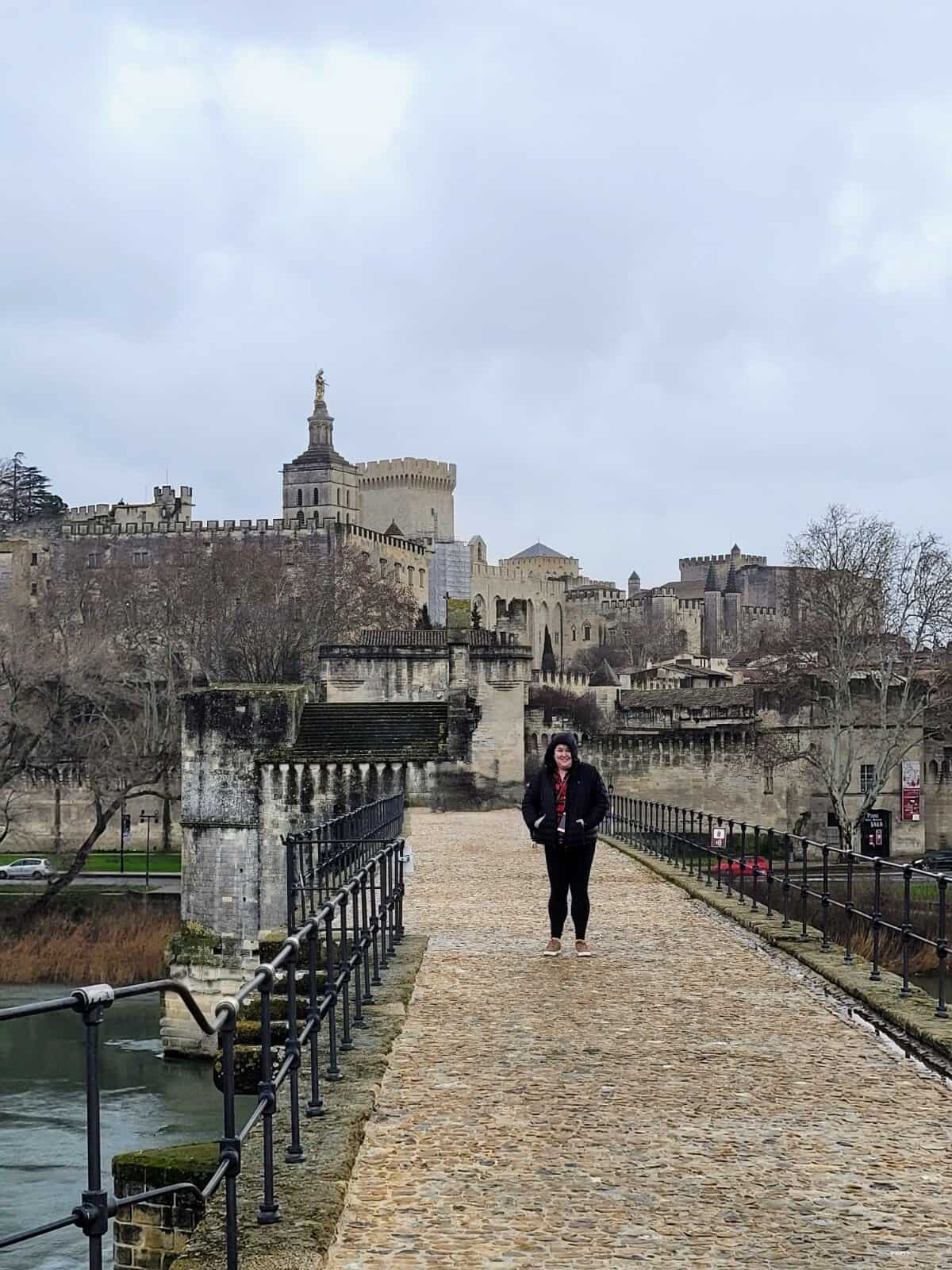 Riana standing on the Pont d'Avignon in the rain with the Palais des Papes behind her