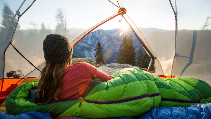 person in sleeping bag looking out of tent