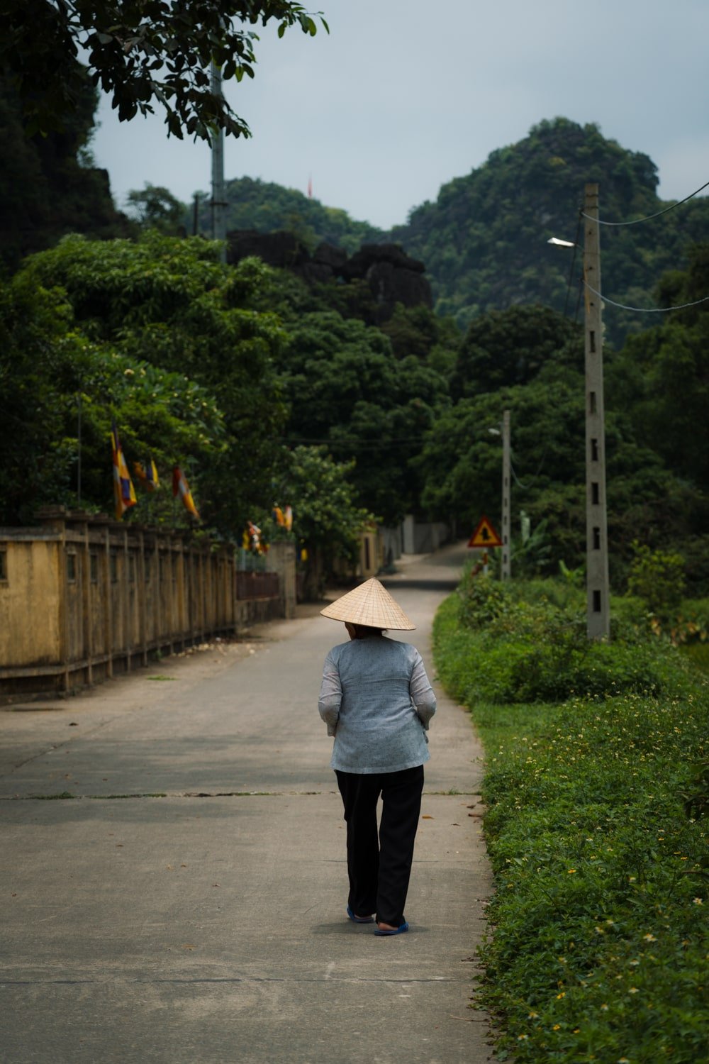 A local Vietnamese woman walking down a countryside road wearing a Vietnamese hat.