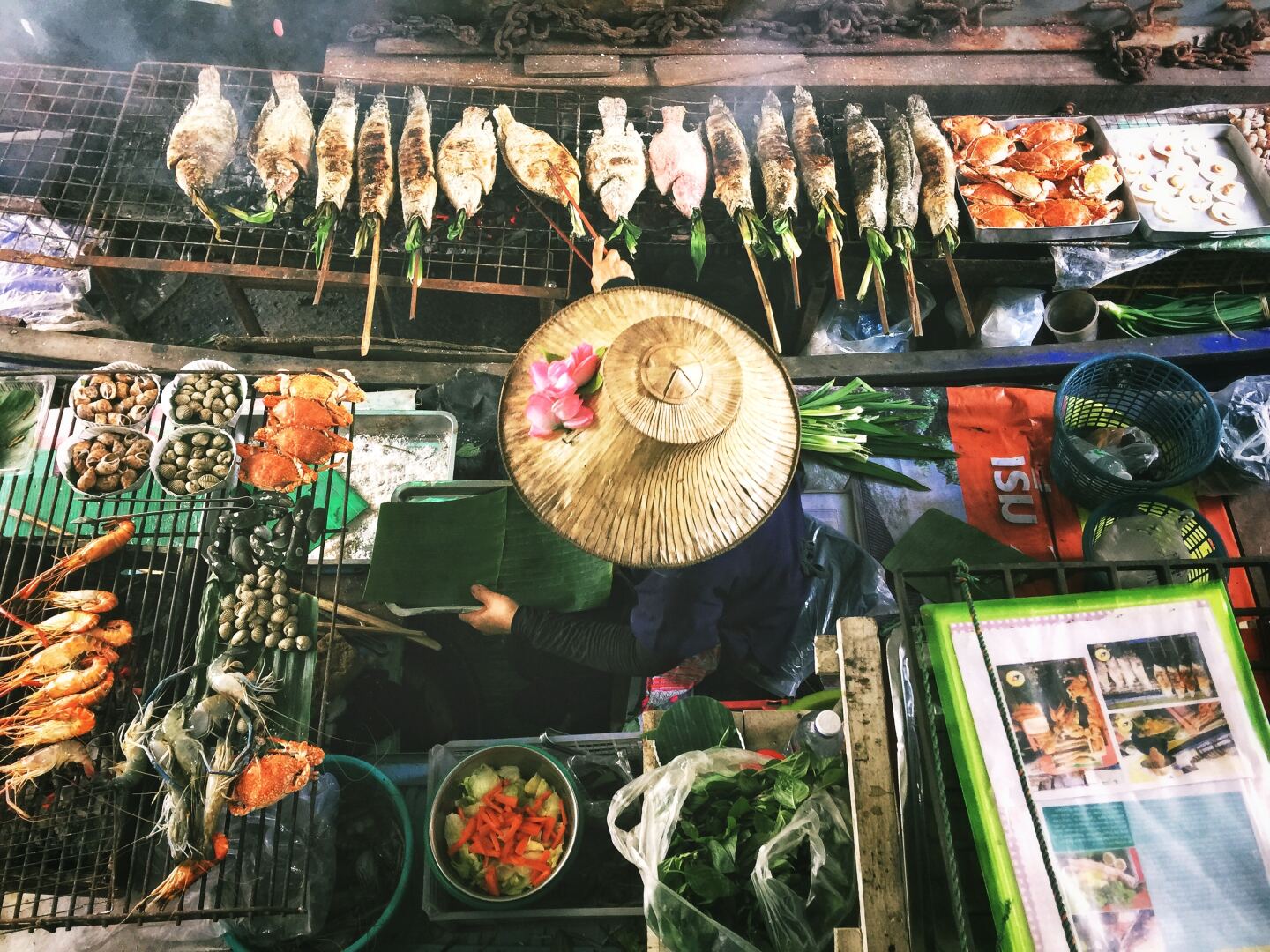 Overhead view of of person in Thailand wearing a wide-brimmed hat and surrounded by grilled fish and seafood