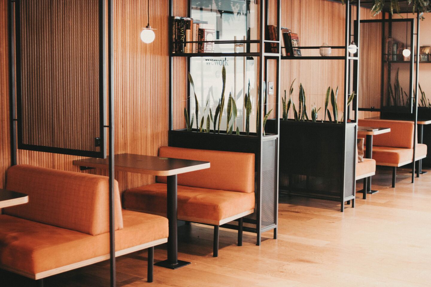 Four empty rust-orange booths divided by tall, linear bookshelves at a WeWork coworking space in Mexico City, Mexico