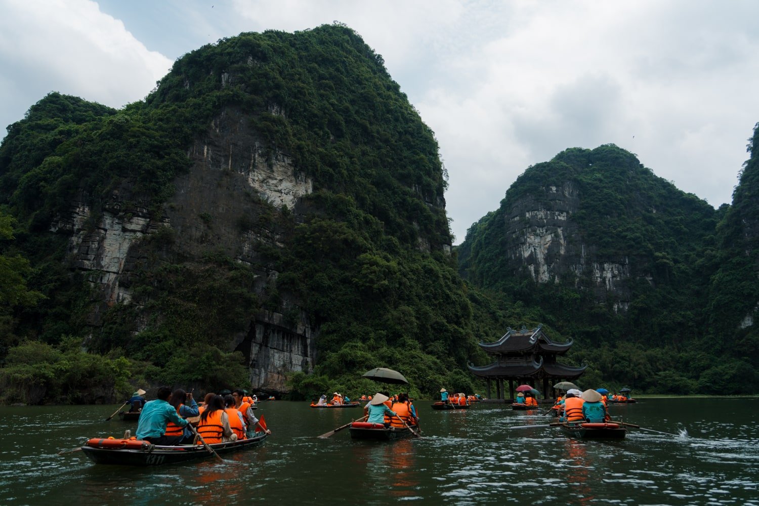 Sightseeing tour boats approach Dia Linh Mountain and Suoi Tien Temple in Trang An, Vietnam.