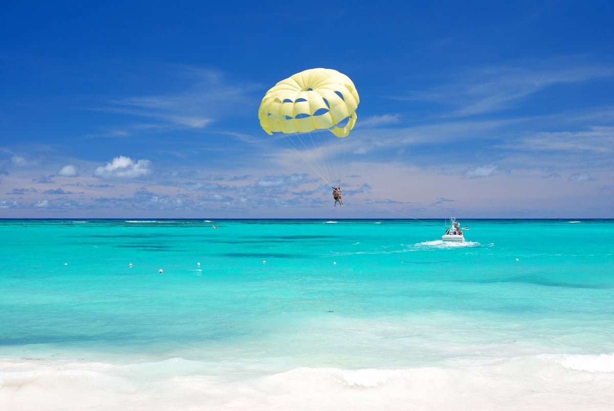 person parasailing on a bright blue ocean water with a yellow parasail. Sunny day.