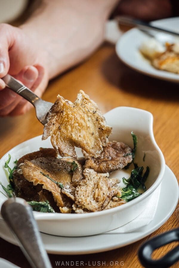 A man holds a fried mushroom on the end of a fork.