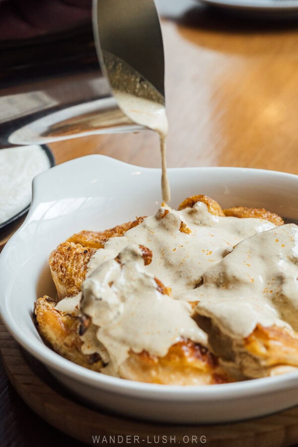 Pouring walnut sauce from a metal jug onto a plate of chicken.