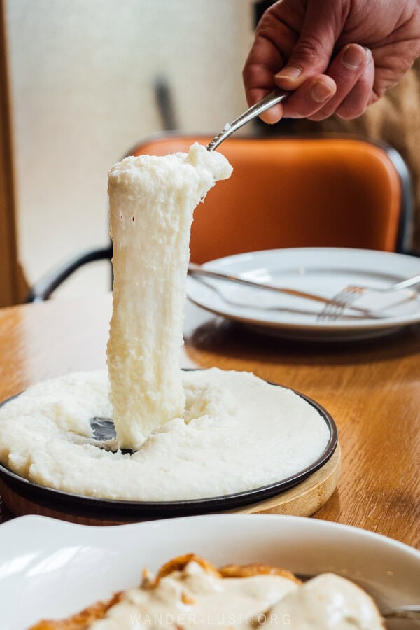 A man stretches a spoonful of elarji, cheesy cornmeal.