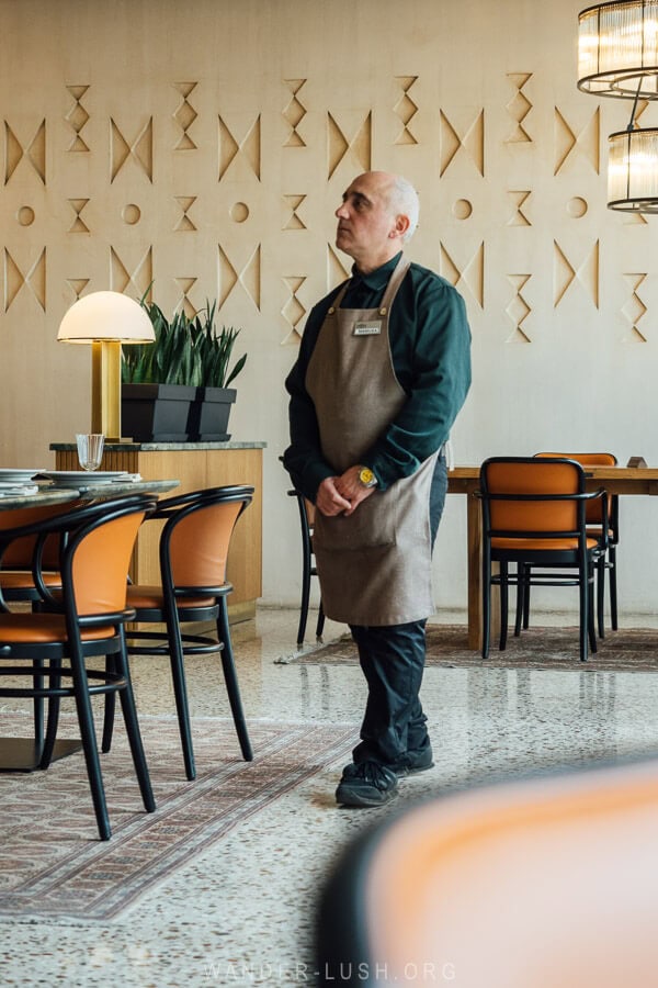 A waiter dressed in green walking through a restaurant dining room.