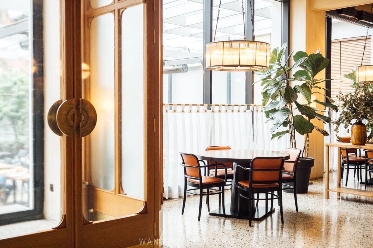 An airy restaurant in Tbilisi with caafe curtains, indoor plants and a Deco-style entry vestibule.