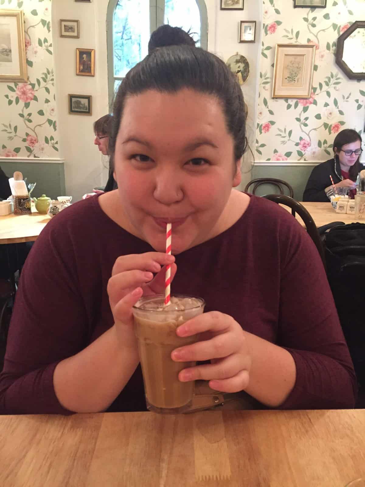 Riana in a London tea shop sipping an iced coffee