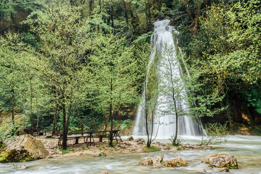 A waterfall surrounded by greenery with a picnic area set up under the trees on the Abasha River near Kutaisi.