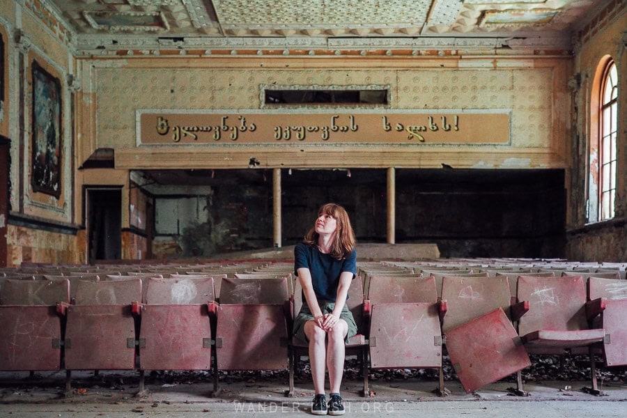 A woman sitting on an old theatre chair inside an abandoned house of culture in Imereti, Georgia.